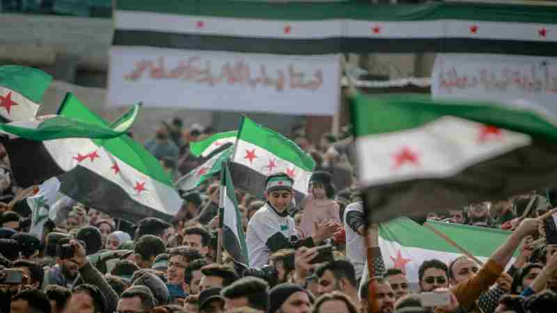 A large crowd protests in Idlib, Syria, waving flags and banners. Energetic and passionate scene., tags: syrer jahrestag des endes von - pexel